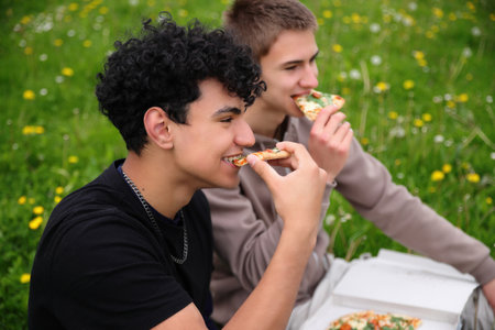 Two friends dining outside, eating pizza in park