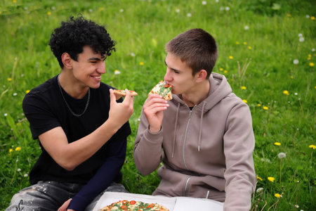 Two friends dining outside, eating pizza in park