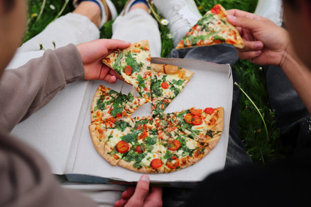 Two friends dining outside, eating pizza in parkの写真素材