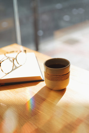 Warm morning light streams across a wooden table illuminating a cup of coffee and an open notebook