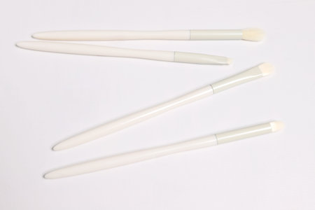 A collection of four pristine white makeup brushes, each featuring a subtle light gray accent on its...