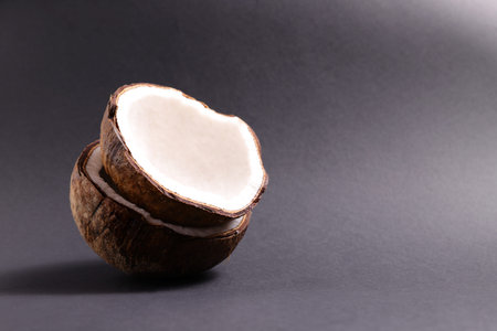 A halved coconut rests on a dark surface, revealing its white interior and textured brown shell