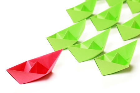 One red and several green paper boats on white backgroundの写真素材