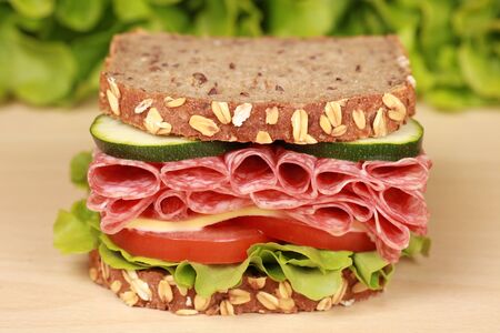 Fresh sandwich with salami, cheese and lettuce on a wooden tableの写真素材