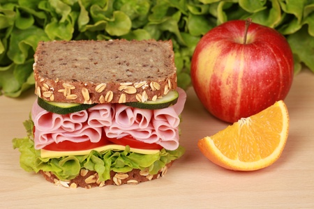 Fresh sandwich with ham, cheese and lettuce, orange and aplle on a wooden tableの写真素材