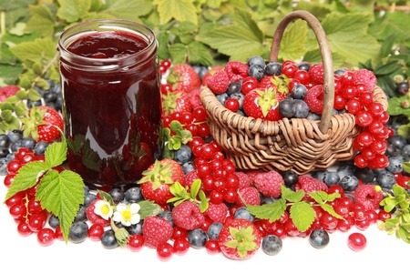 Strawberries, red currants, raspberries and blueberries on white with a basket and a marmalade jarの写真素材