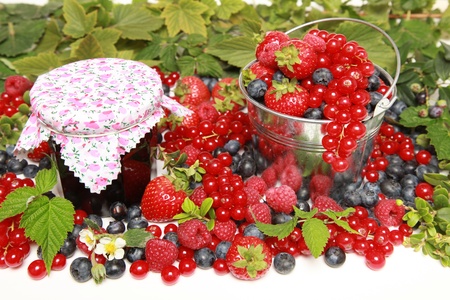 Strawberries, red currants, raspberries and blueberries on white with a bucket and a marmalade jarの写真素材