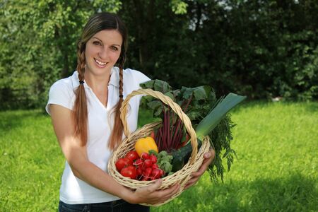 A young woman is holding a basket with fresh vegetablesの写真素材