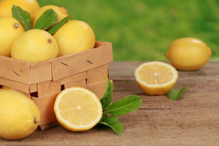 Lemons with leaves in a wooden box on a table with green background の写真素材