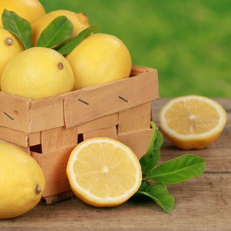 Lemons with lemon leaves in a wooden box on a table with green backgroundの写真素材