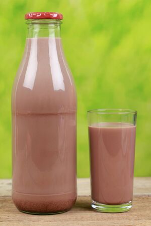 Chocolate drink in a bottle and in a glass with a green backgroundの写真素材
