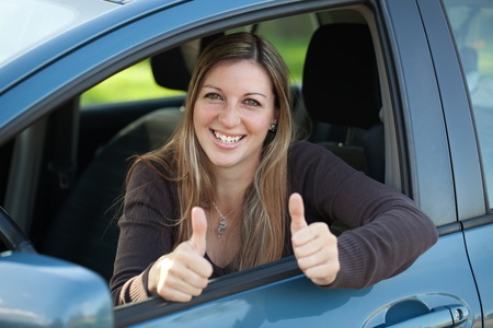 A happy female driver leaning out of the window and showing both thumbs upの写真素材