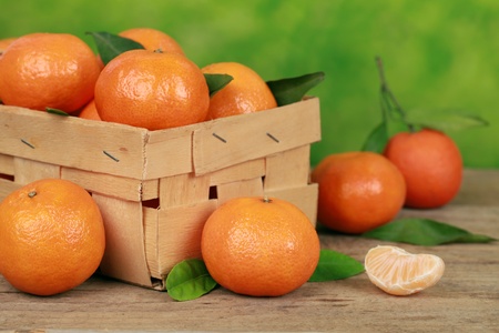Tangerines with leaves in a wooden box on a table with green background の写真素材