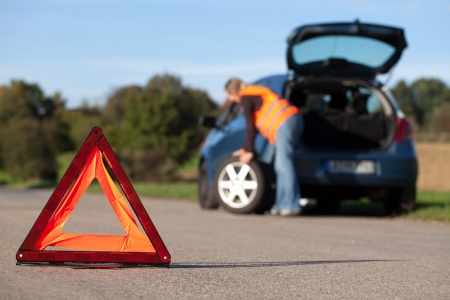 Tire change on a broken down car with a red warning triangleの写真素材