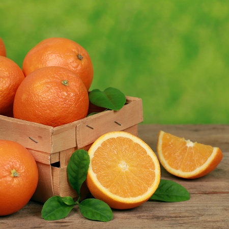Freshly picked oranges with leaves in a wooden box on a table with green background の写真素材