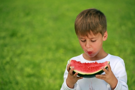 Young boy eating a watermelon with stains on his shirtの写真素材
