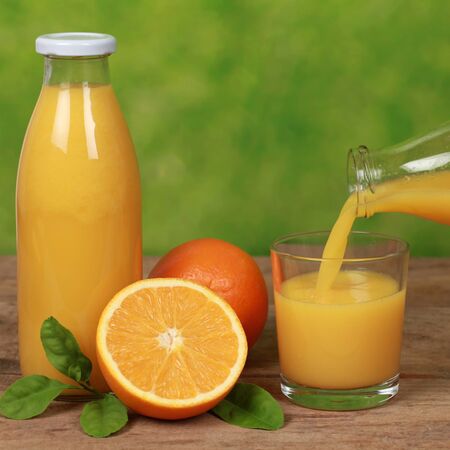 Oranges and fresh juice is pouring from a bottle into a glass on a wooden tableの写真素材