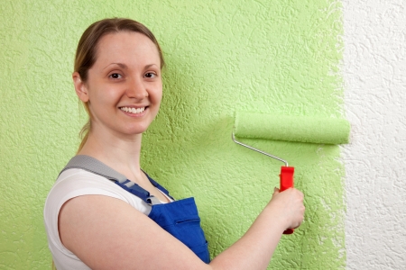 Young woman painting a wall with a paint rollerの写真素材