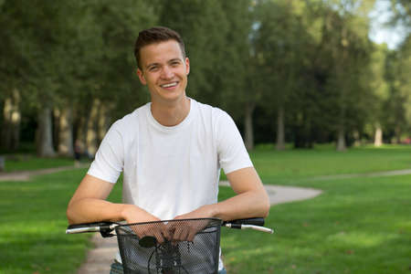 Young man leaning against a bike in a parkの写真素材