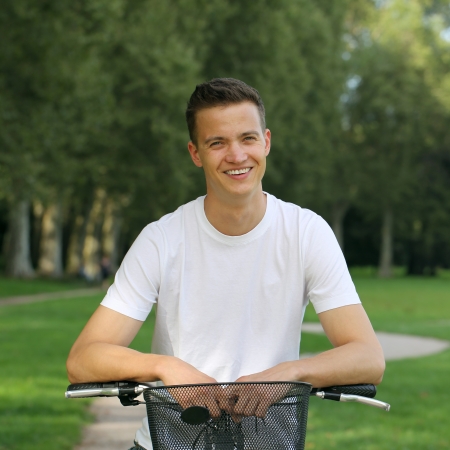 Smiling young man leaning against his bike in a parkの写真素材