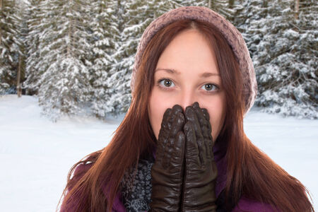 Young woman with gloves and cap freezing in winter in a forest with snowの写真素材