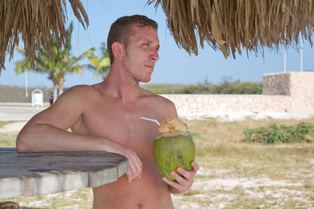 Young man on vacation on the beach drinking from coconutの写真素材