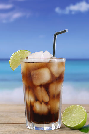 Cold cola drink in glass with ice cubes and lime on the beachの写真素材