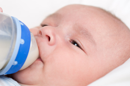 A small baby is hungry and drinking milk from a bottleの写真素材