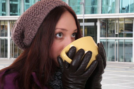 Young woman drinking cup of tea in winter and looking up outdoors in townの写真素材