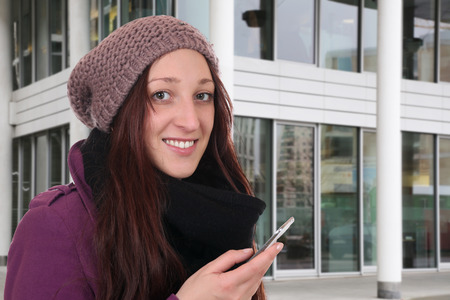 Young woman in winter making a call with a smartphone or mobile phone outdoor in townの写真素材