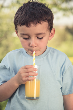 Child kid little boy drinking orange juice drink outdoor vintage look portrait format outdoors outside glassの写真素材