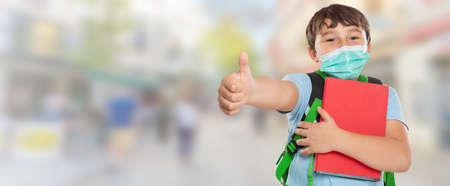 Young student child kid little boy wearing face mask against virus showing thumbs up in townの写真素材