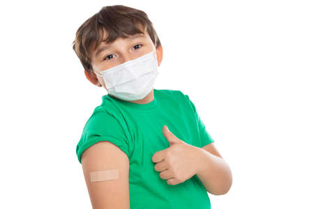 Child kid with plaster after virus vaccination wearing face mask against Virus showing thumbs up isolated on a white backgroundの写真素材