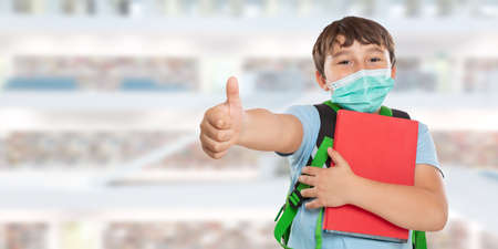 Young student child kid little boy at school wearing face mask against virus showing thumbs upの写真素材