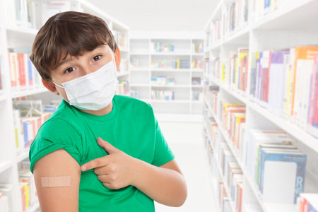 Child kid pointing on plaster after virus vaccination at school wearing face mask against Virus  copyspace copy space latinの写真素材