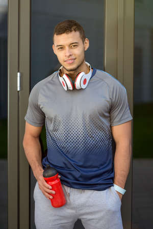 Smiling young latin man water bottle runner portrait format sports fitness training outdoorの写真素材