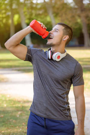 Runner smiling young latin man drinking water running portrait format sports training fitness workout outdoorの写真素材