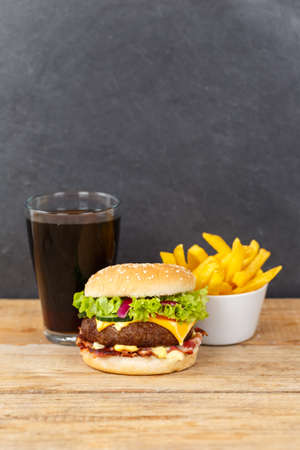 Hamburger Cheeseburger meal fast food with cola drink and French Fries on a wooden board portrait format menuの写真素材