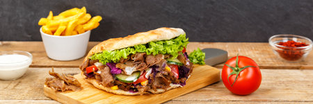 Doner Kebab Doner Kebap fast food meal in flatbread with fries on a wooden board panorama boardの写真素材