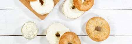 Bagel sandwich with fresh cream cheese for breakfast from above panorama on a wooden boardの写真素材