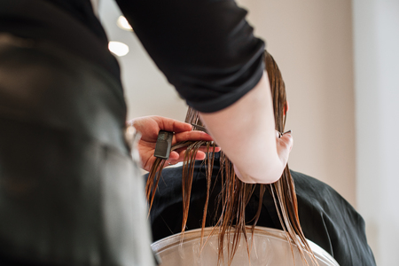 Close-up of stylist hairdresser doing haircut for the girl with wet brown hair. Comb, scissors. working equipment. Split ends cut concept.の写真素材