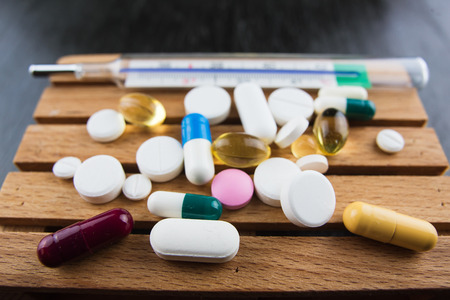 Closeup of thermometer and colorful pills. Illness and sickness concept. Remedy on black backgroundの写真素材