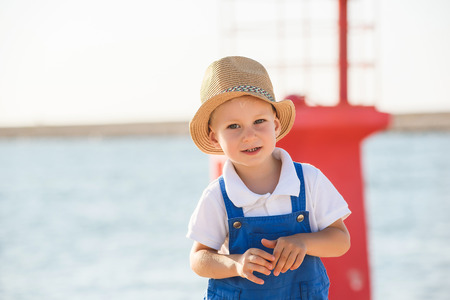 Happy cute small blond boy with blue eyes in a blue overall, white shirt and playing in port on a...