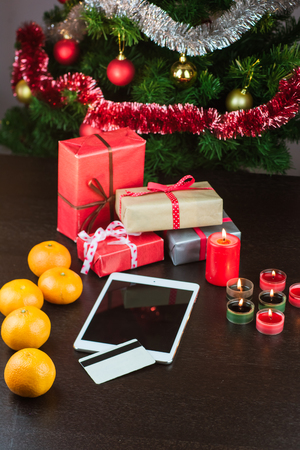 Close-up of tablet and credit card lying on table with mandarins, presents and Christmas tree. Online Christmas shopping concept. Christmas and New Year holidaysの写真素材