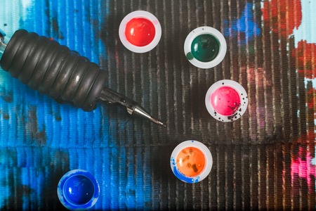 Tattoo artist table with tattoo machine, gun, inks and tablecloth with stains. Small cups with colorful inks.の写真素材