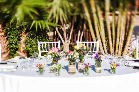 Close-up of small colorful bouquets in decorated vases. Outdoor wedding celebration at a restaurant....