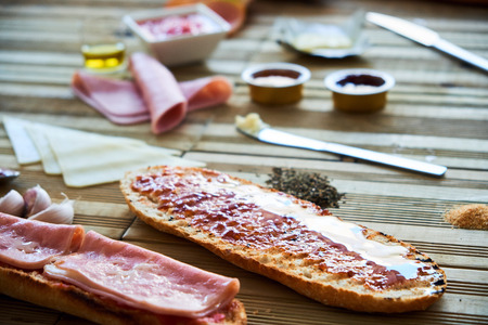 Close-up of delicious toasts and ingredients. Ham york, cheese, tomato, oil, jam and butter on...