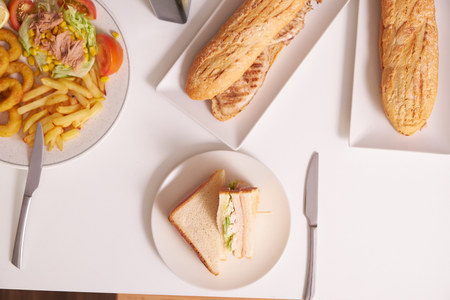 French fries, salad, sandwiches, fried squid and eggs on white table, overhead view.の写真素材