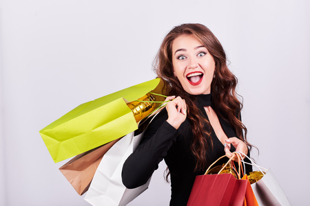 Portrait of a young surprised woman with open mouth carrying colorful shopping bags on shoulder on white background. Sales and black friday concept.の写真素材