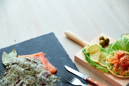 Tasty fresh salted salmon fillet with crispbread and avocado on wooden board. Aromatic herbs, spices and vegetables - healthy food, diet and cooking concept.の写真素材